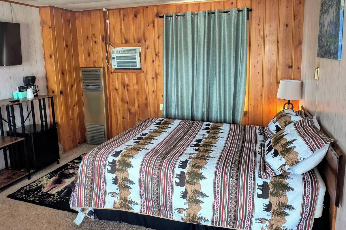 A room with a bed, a desk, a coffee maker, an air conditioner, and a wall-mounted TV.