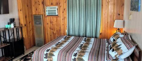 Una habitación con cama, escritorio, cafetera, aire acondicionado y televisor montado en la pared.