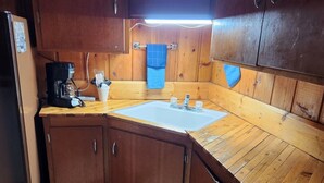 A compact kitchen with wooden cabinets, a sink, and a coffee maker. - Big Sky Motel (Choteau)