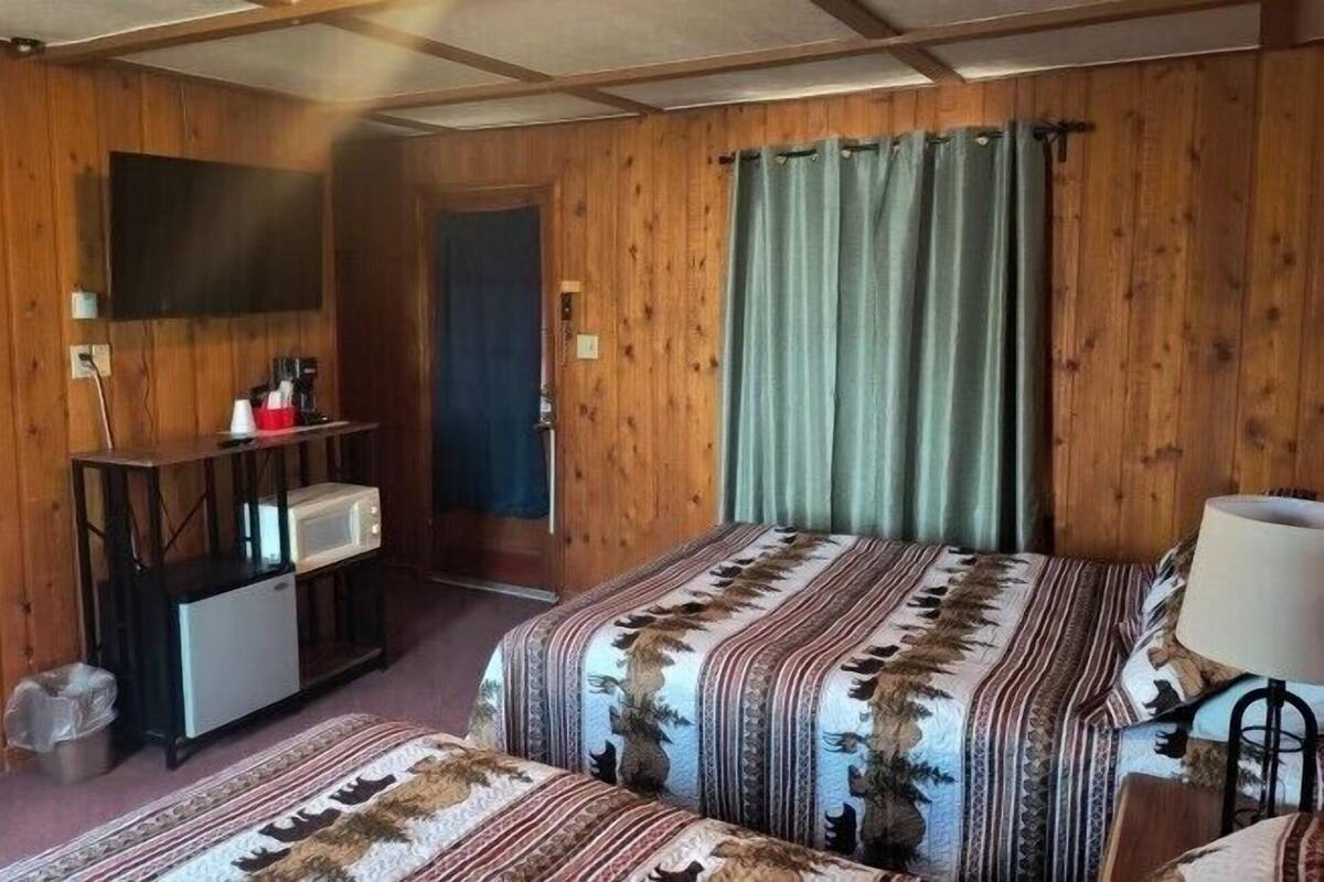 A room with wooden walls, a bed with patterned bedding, a small desk with a microwave, and a television mounted on the wall.