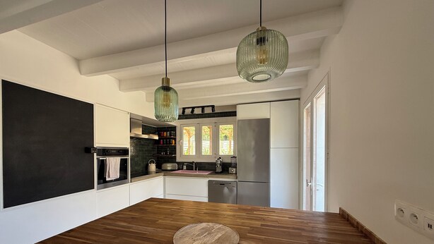 A modern kitchen with a wooden floor, a round wooden table, and a hanging green pendant light. - Villa Sunset 500 meters Ocean (Seignosse)