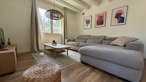 A modern living room with a grey sofa, a wooden coffee table, a woven ottoman, and a large window with curtains. - Villa Sunset 500 meters Ocean (Seignosse)