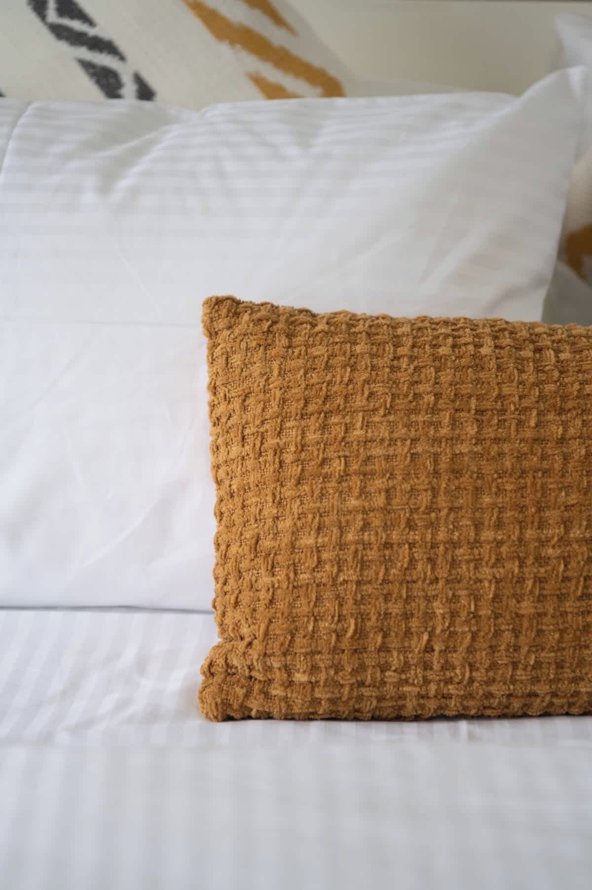 A bed with white sheets and a textured brown pillow.