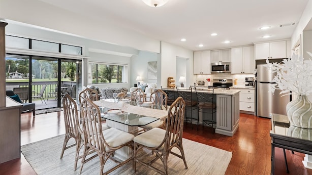 A modern kitchen with white cabinets, stainless steel appliances, and a dining area with glass tables and wicker chairs.
