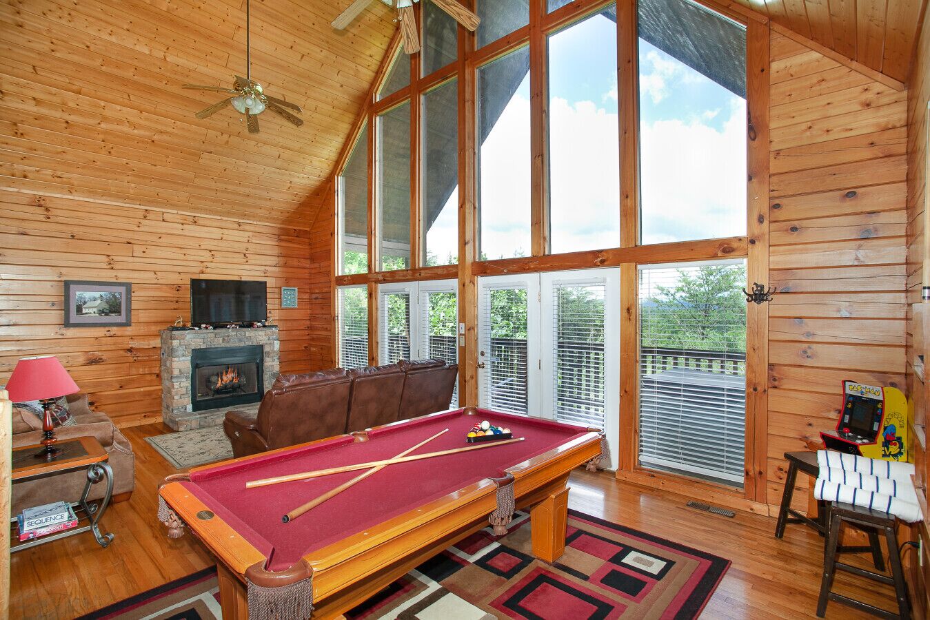 A cozy cabin interior with a pool table, a fireplace, and large windows offering a view of the outdoors.