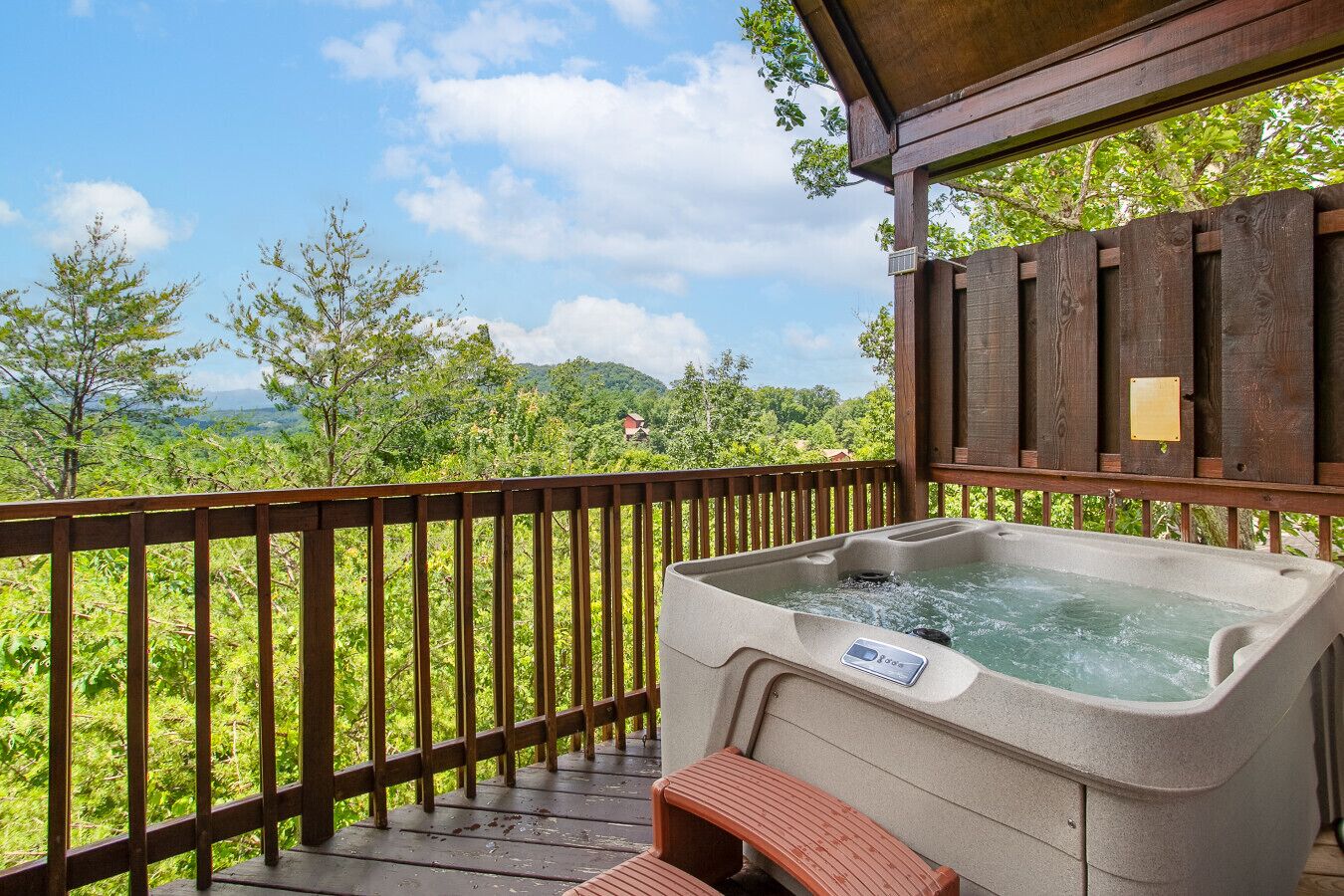 A hot tub on a wooden deck with a view of a forest and mountains.