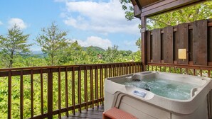 A hot tub on a wooden deck with a view of a forest and mountains.