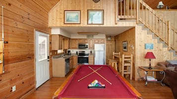 A cozy cabin with a pool table, wooden interior, kitchen, and a staircase leading to a loft.