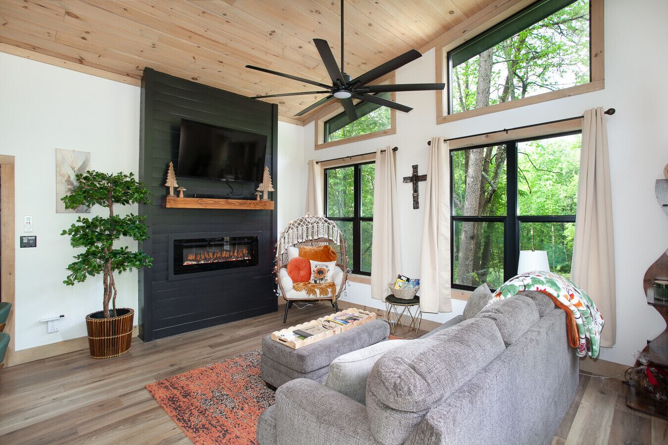 A cozy living room with a fireplace, a large window, and a ceiling fan.
