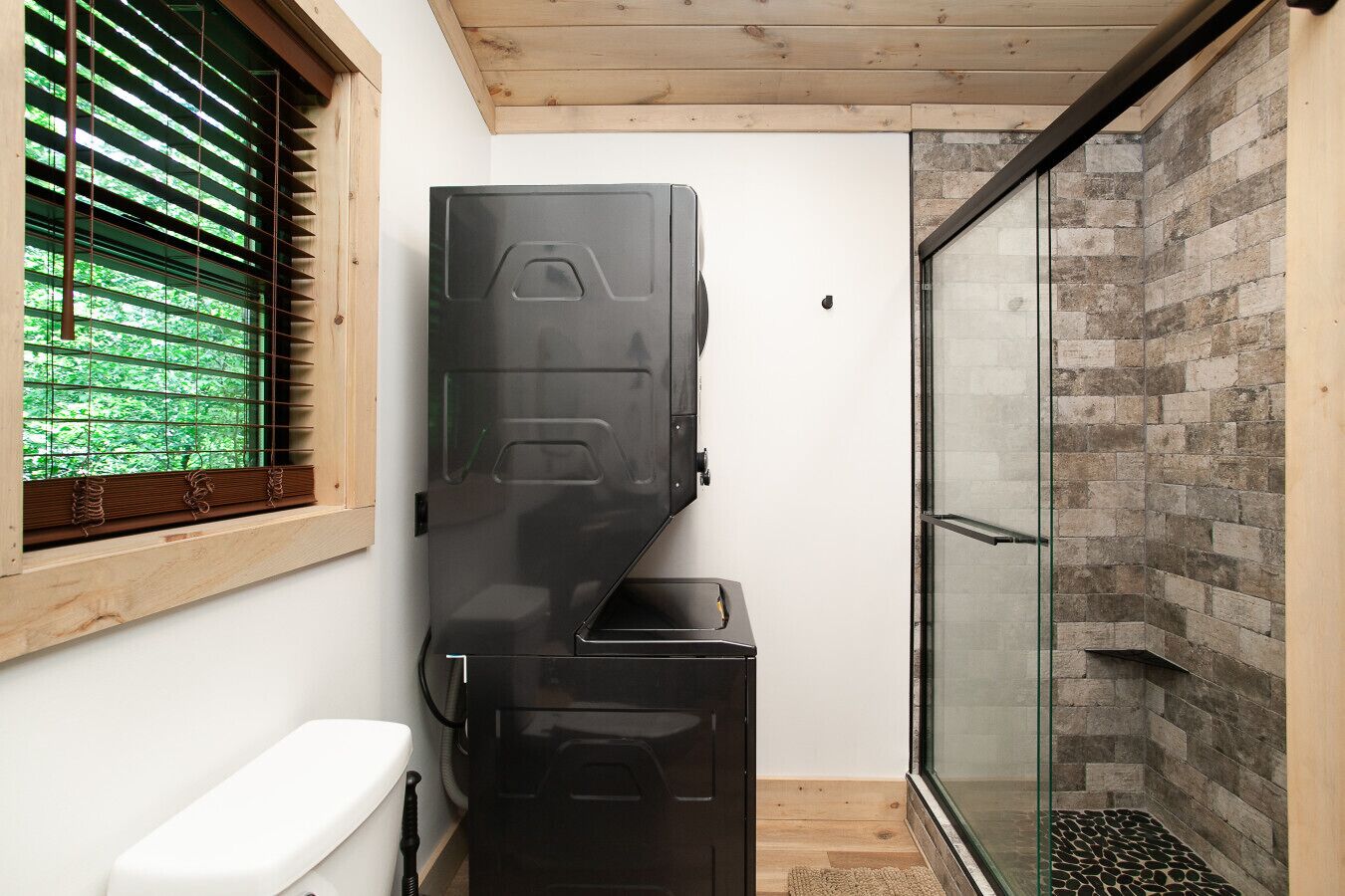 Une petite salle de bain comprenant des toilettes, un meuble noir et une douche en verre avec des carreaux de pierre.