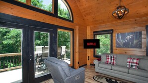 Een gezellig interieur van een chalet met een grijze bank, een grijze fauteuil en een groot televisiescherm waarop 'NETFLIX' staat.