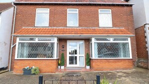 A two-story brick house with a tiled roof, large windows with metal grilles, and a front door with a small porch area. - Highland House (Sheringham)