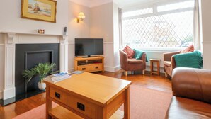 A living room with a fireplace, a television on a wooden stand, a sofa, a coffee table, and a window with a view. - Highland House (Sheringham)