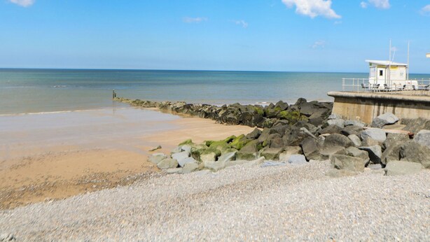A beach with a rocky breakwater and a lifeguard tower. - Highland House (Sheringham)
