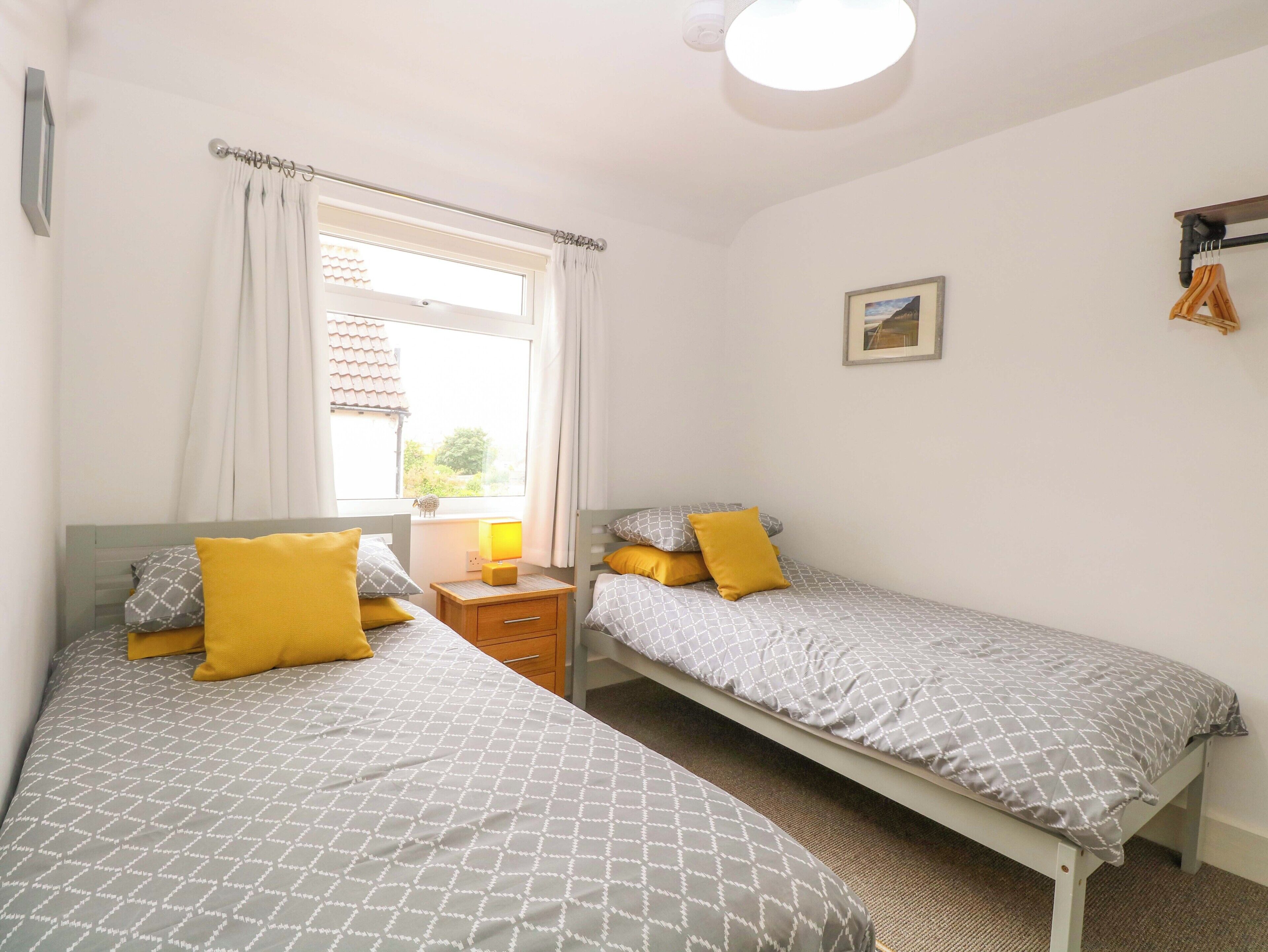 Une chambre avec deux lits, une fenêtre avec des rideaux, une table de chevet avec une lampe et un tableau au mur.