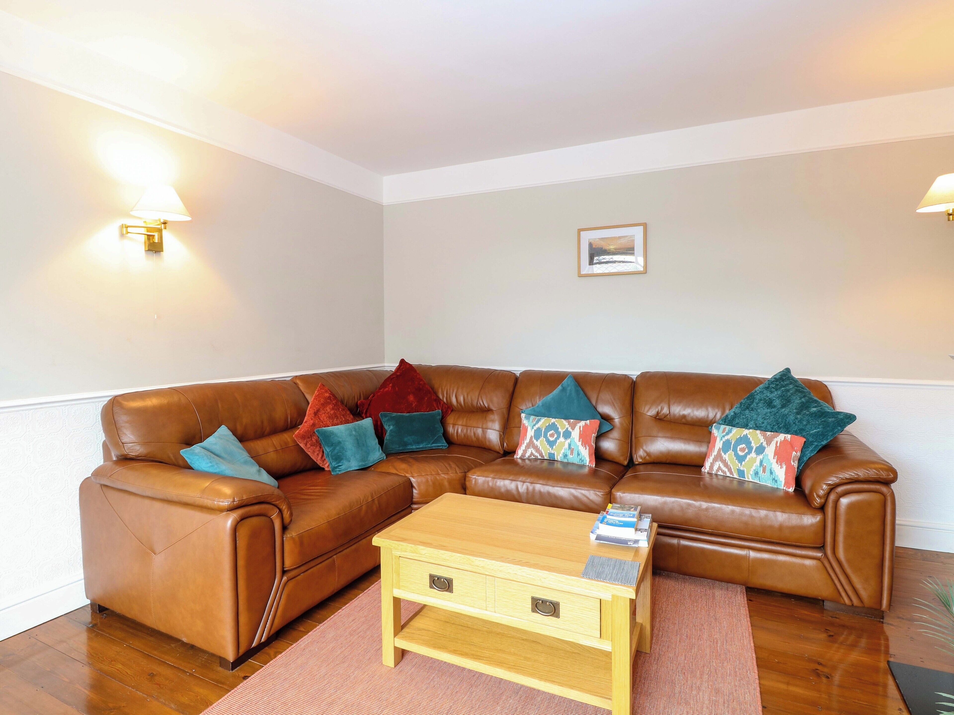 A brown leather sofa with colorful cushions, a wooden coffee table, and two wall-mounted lamps.