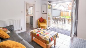 A living room with a sofa, a wooden bench, and a table with a polka dot tablecloth. There is a sliding glass door leading to a patio with outdoor furniture. - Highland House (Sheringham)
