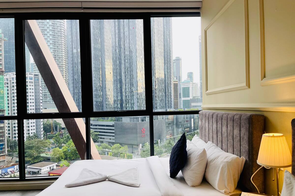 Een hotelkamer met een groot raam met uitzicht op hoge gebouwen en een stadsbeeld.