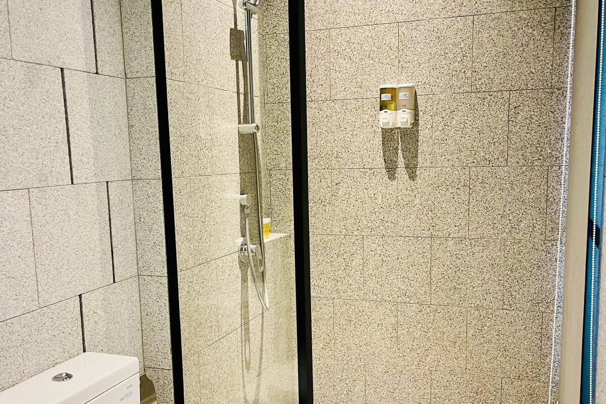 Een moderne badkamer met een toilet, een douchecabine van glas en een zeepdispenser op de muur.