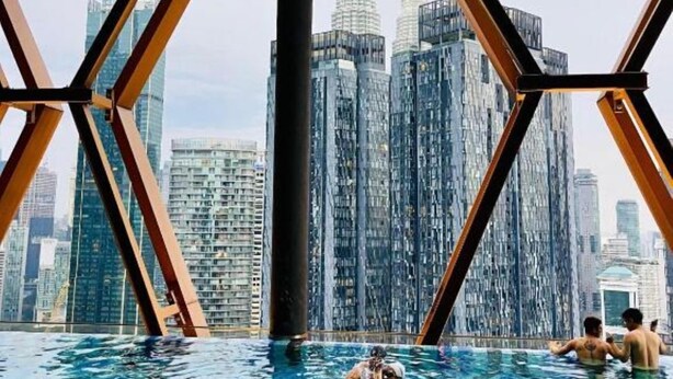 An indoor swimming pool with a view of tall buildings, including a distinctive tower with two spires. - Scarletz KLCC By Arman (Kuala Lumpur)