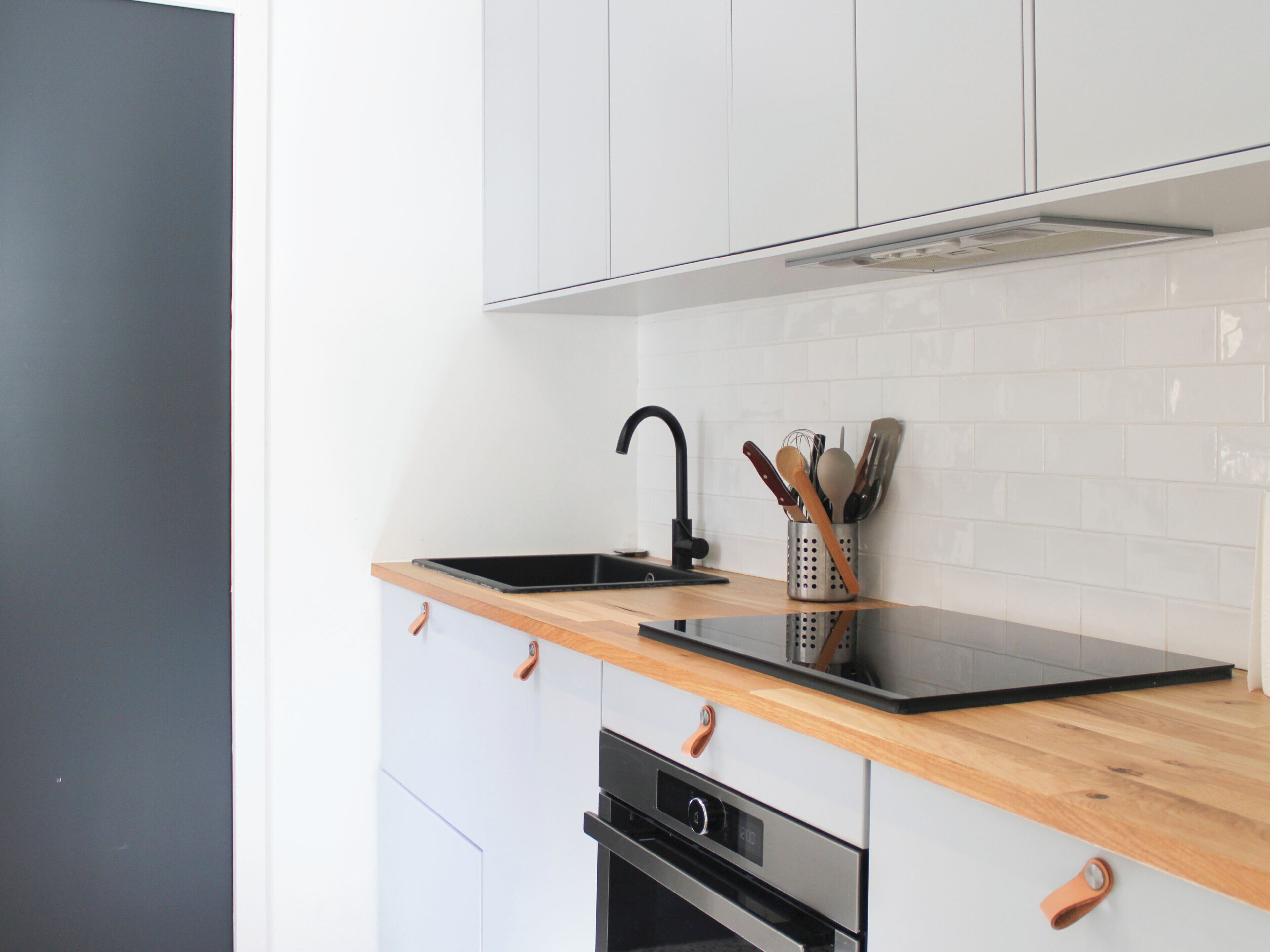 A modern kitchen with a black sink, wooden countertop, stainless steel oven, and white cabinets.