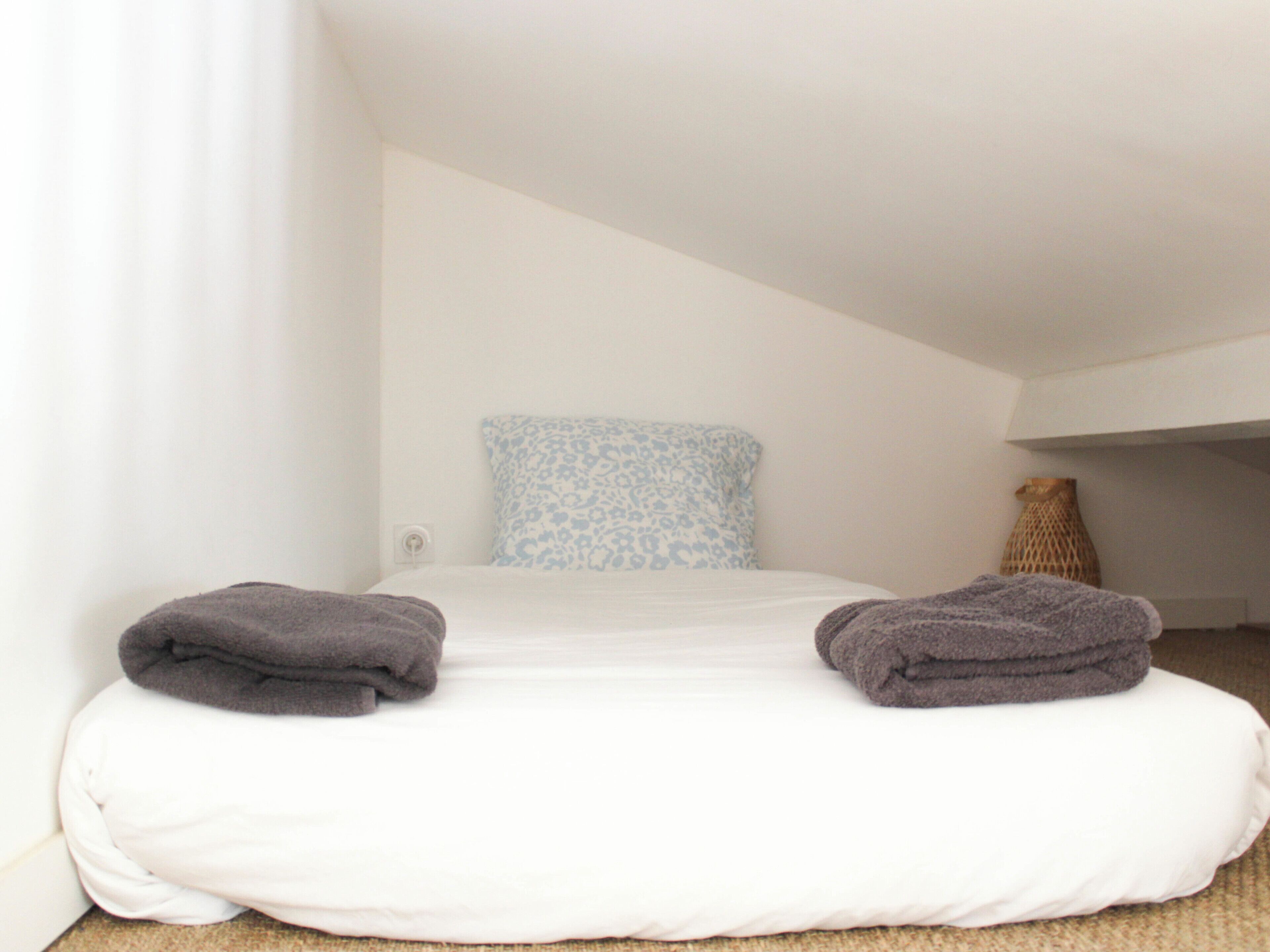 A bedroom with a bed, pillows, a vase, and a blanket.
