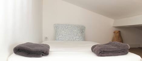 A bedroom with a bed, pillows, a vase, and a blanket.