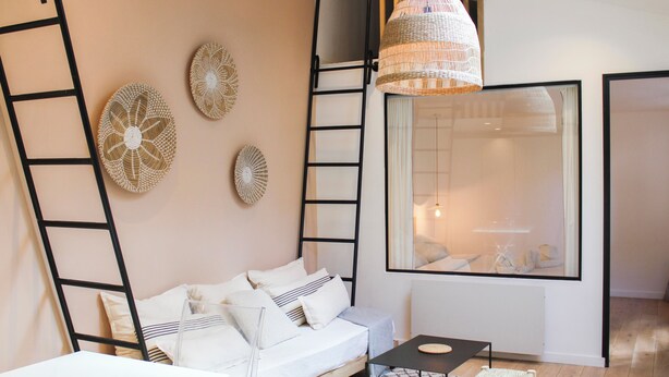 Un salon moderne avec un canapé blanc, une table basse noire et un luminaire suspendu en fibres tressées.