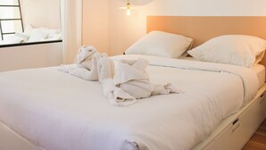 Un lit bien fait, avec des draps blancs et une serviette posée sur le dessus, une lampe de chevet et une fenêtre avec des rideaux.