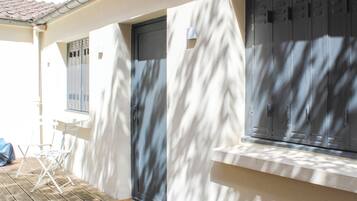 A covered outdoor area with a wooden floor, a door, and a window with blinds.