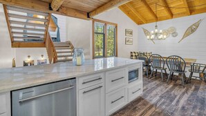 A modern kitchen with a large island, wooden ceiling beams, and a dining area with vintage chairs. - Charming 2-Bedroom Condo with Golf Course Views – Ideal for Families or Couples (Sunriver)