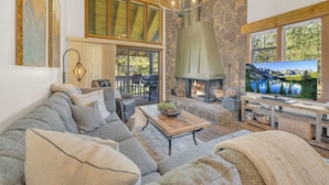 A cozy living room with a stone fireplace, a large TV, and a comfortable seating area. - Charming 2-Bedroom Condo with Golf Course Views – Ideal for Families or Couples (Sunriver)