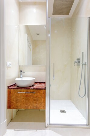 Un baño moderno con ducha envuelta en vidrio, tocador de mármol y un espejo grande.