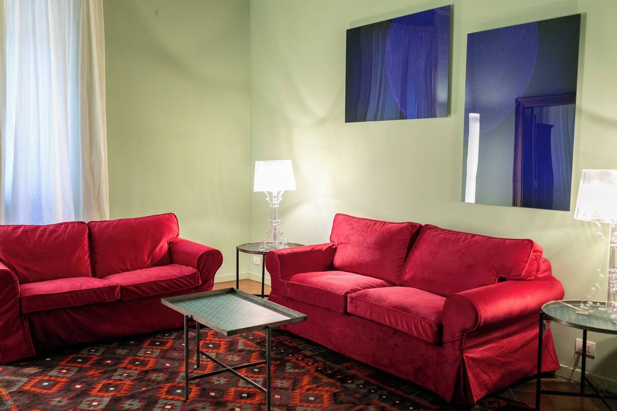 Une pièce avec deux canapés rouges, une petite table, un tapis à motifs et deux lampes fixées au mur.