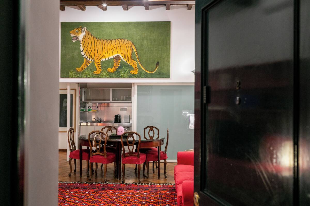 Un coin repas avec un canapé rouge, une table et des chaises. Un grand tableau représentant un tigre est accroché au mur.