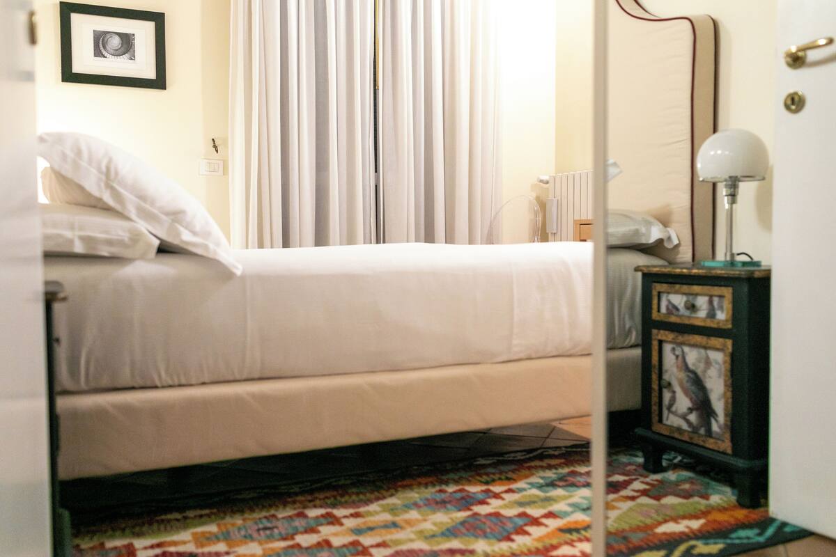 Une chambre à coucher avec un lit, une table de chevet avec une lampe, un tableau encadré et un tapis coloré.