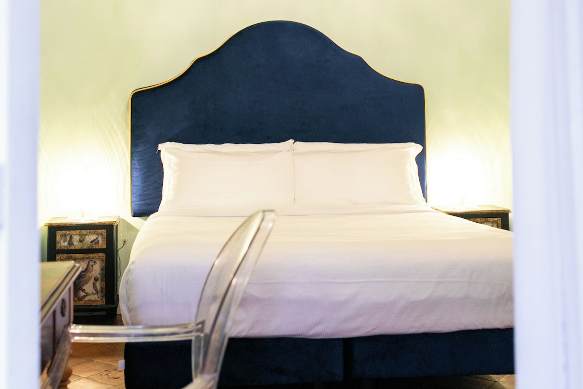 Une chambre à coucher avec un grand lit, un lustre et une table de chevet sur laquelle est posé un cadre photo.