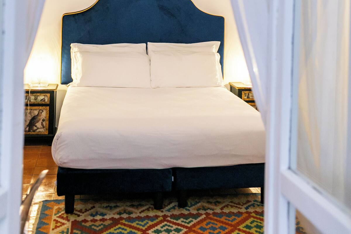 Une chambre à coucher avec un lit, des rideaux blancs, un lustre et un tapis à motifs.
