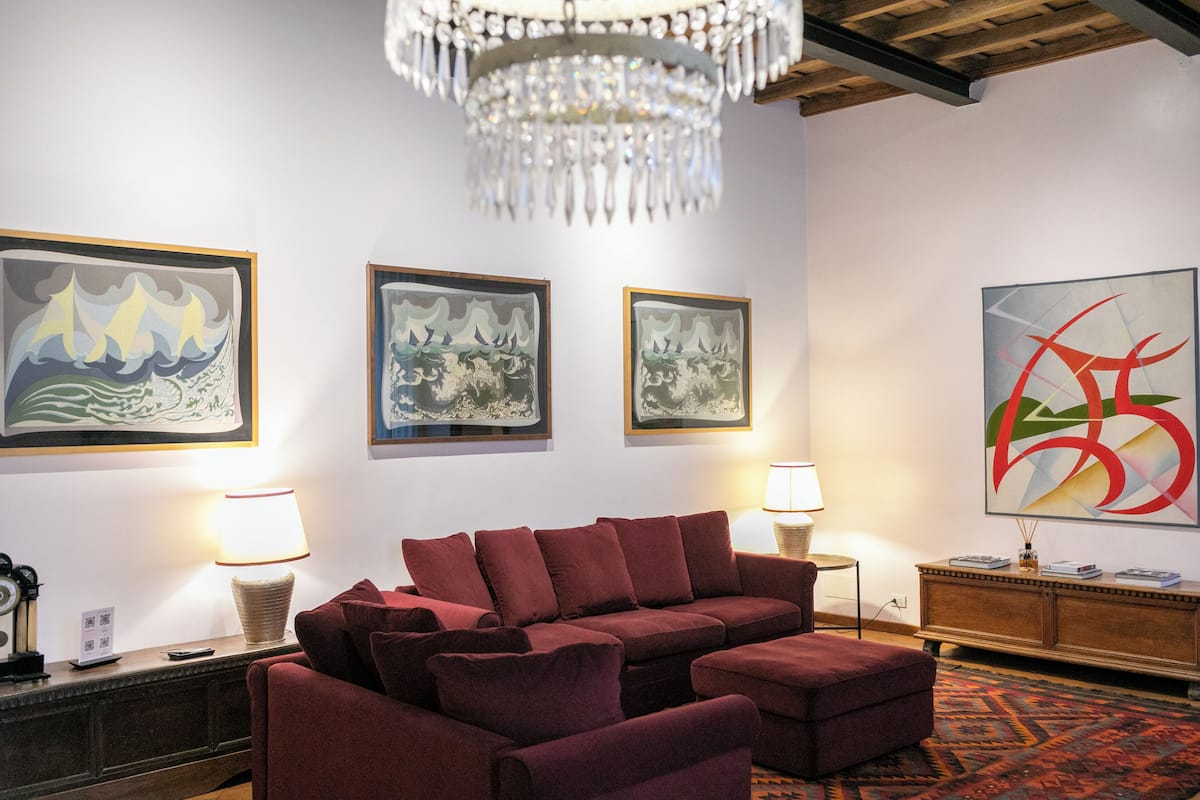 Un salon avec un canapé rouge, un lustre et trois tableaux abstraits encadrés accrochés au mur.