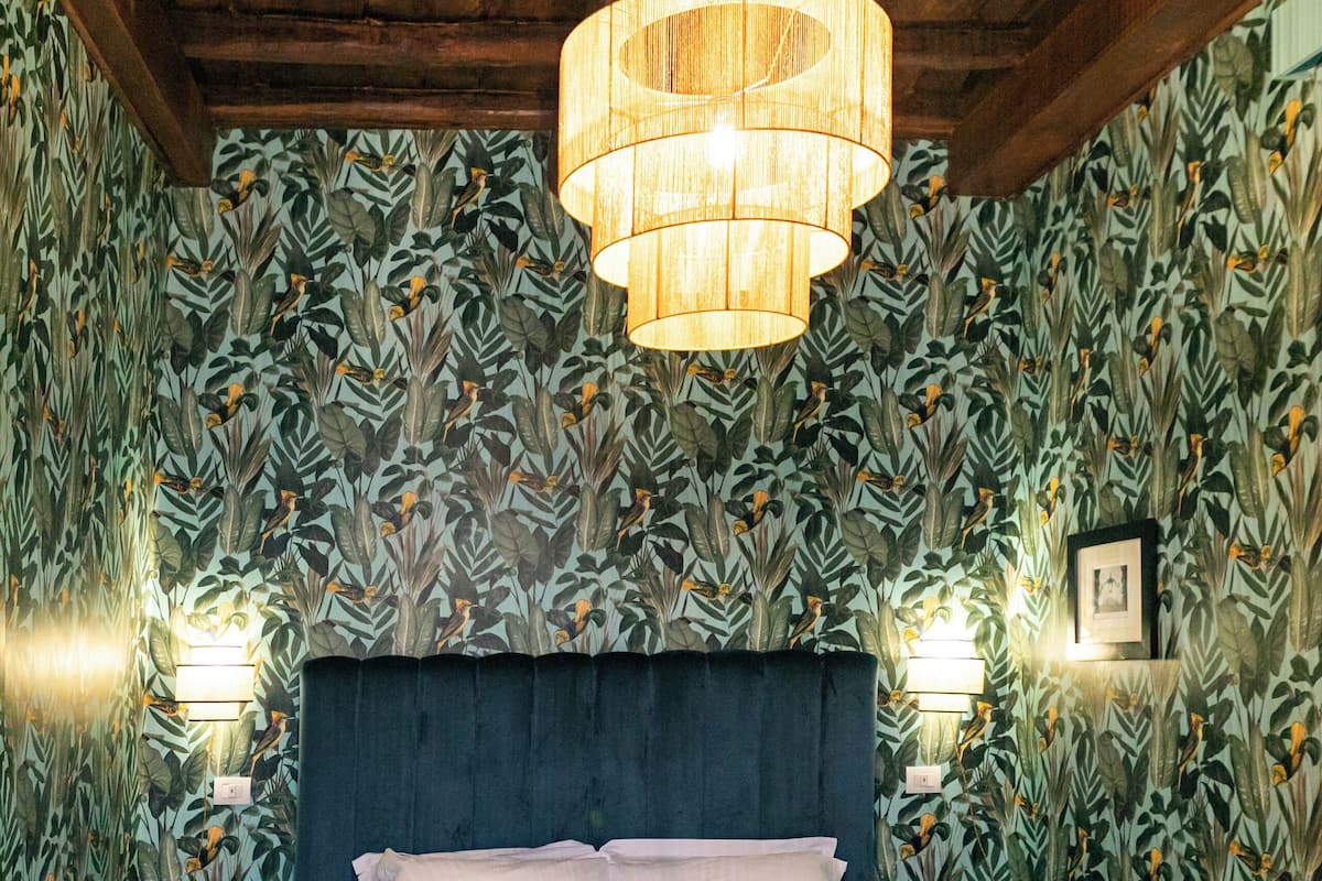 Une chambre à coucher avec un grand lit, des poutres apparentes en bois au plafond et un papier peint à motifs.