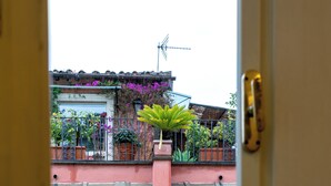 A view through a window of a building with multiple balconies, each adorned with potted plants and flowers. - InCentrum    (Rome)