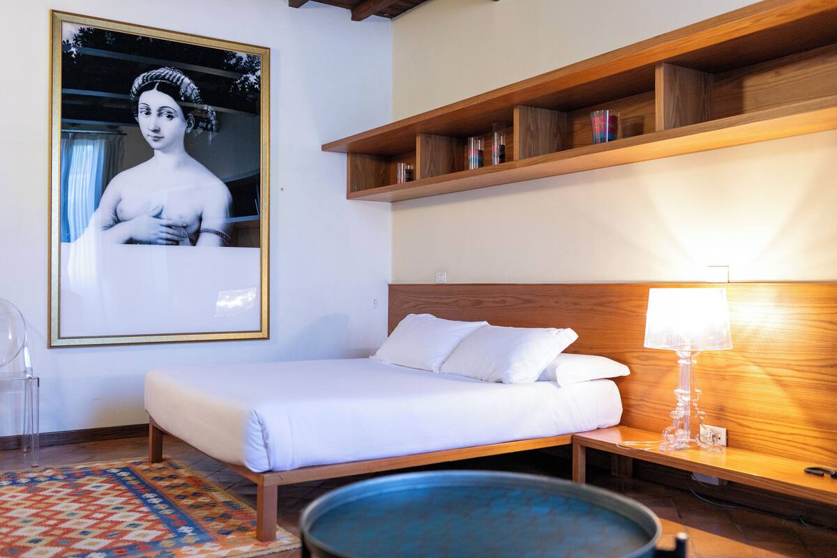 Une chambre bien rangée, avec un lit, une table de chevet, une lampe et une étagère ornée d’objets décoratifs.