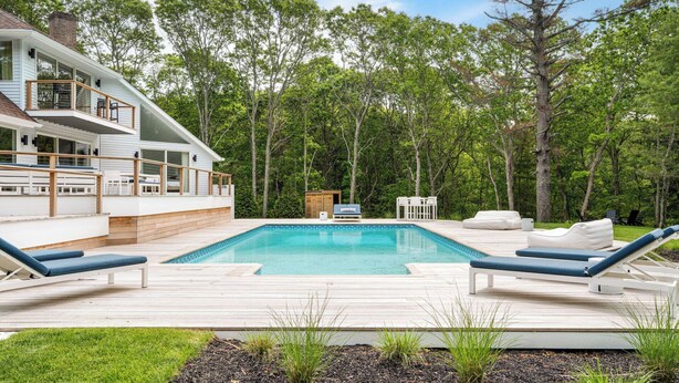 Una casa moderna con piscina, sillas de deck y vistas a un bosque.