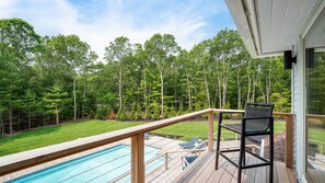Una terrazza con piscina, una sedia e vista su una foresta.