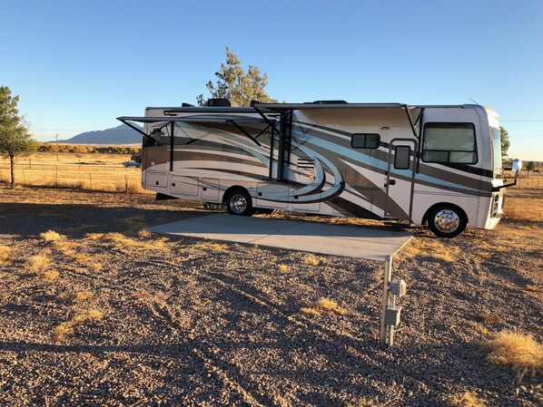 A recreational vehicle parked in a dry, open field with a mountainous backdrop.
