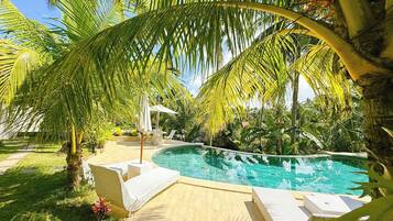 A private pool area with lounge chairs and a small table, surrounded by palm trees and greenery.
