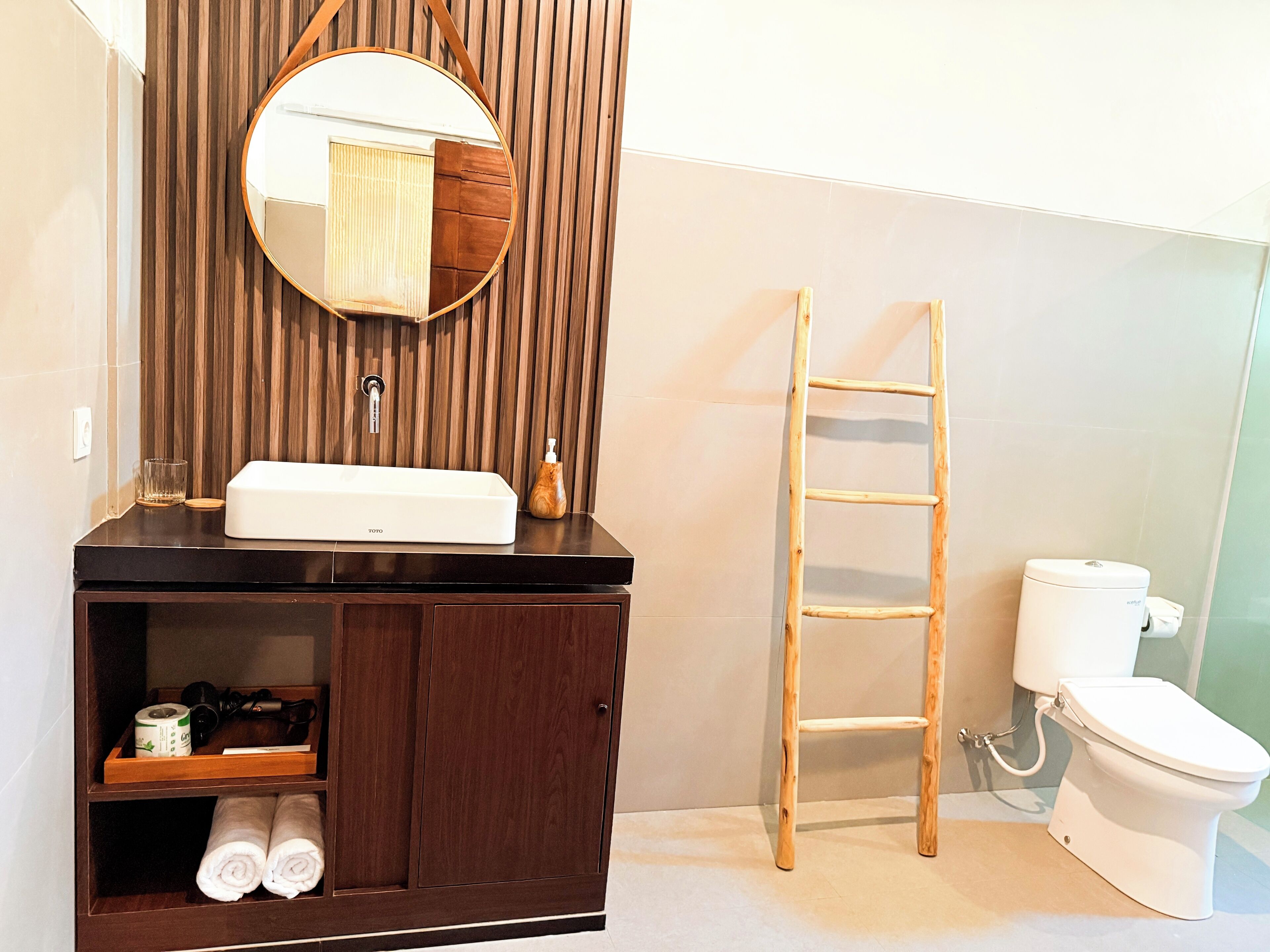 Un baño con tocador de madera, un espejo, inodoro y una escalera de madera.
