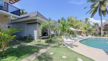 A modern house with a swimming pool, surrounded by palm trees and a well-maintained lawn.