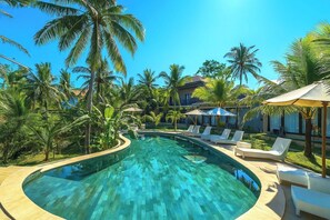 Piscina con sillones de descanso y palmeras, rodeada por un edificio de resort.
