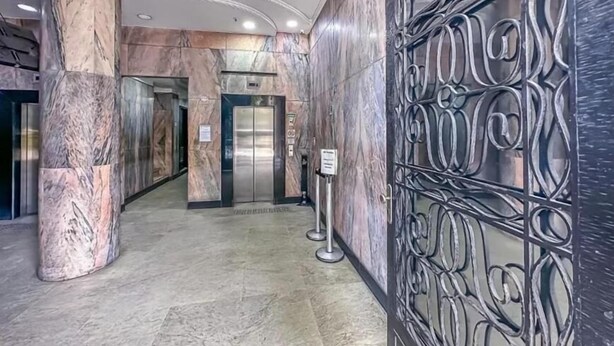 Un pasillo con suelo de mármol, ascensores y un panel decorativo de metal a la derecha.